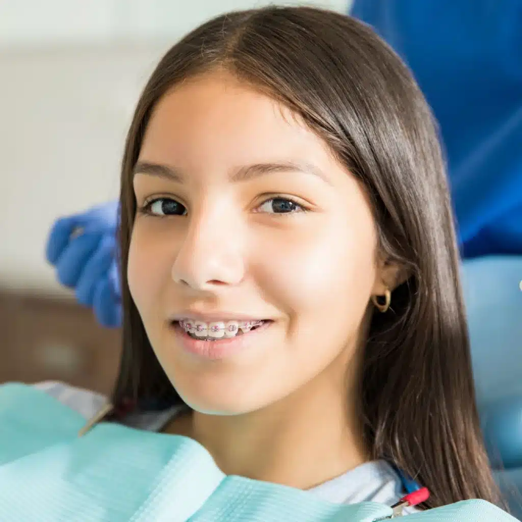 Smiling teenage girl wearing braces with dentist standing in the background
