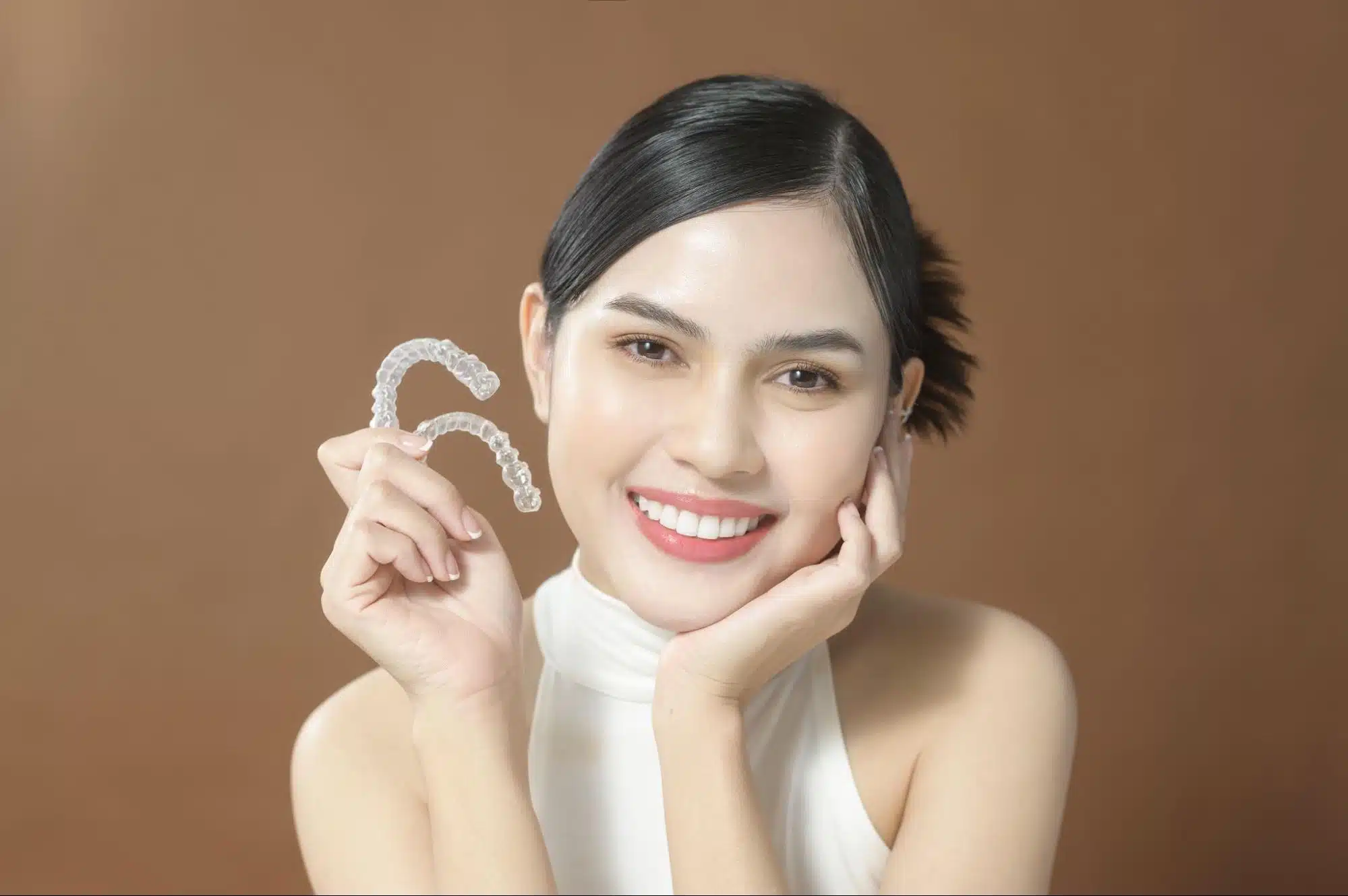 young-woman-holding-invisalign-clear-aligner Young woman smiling, holding clear Invisalign aligner, showing straight teeth
